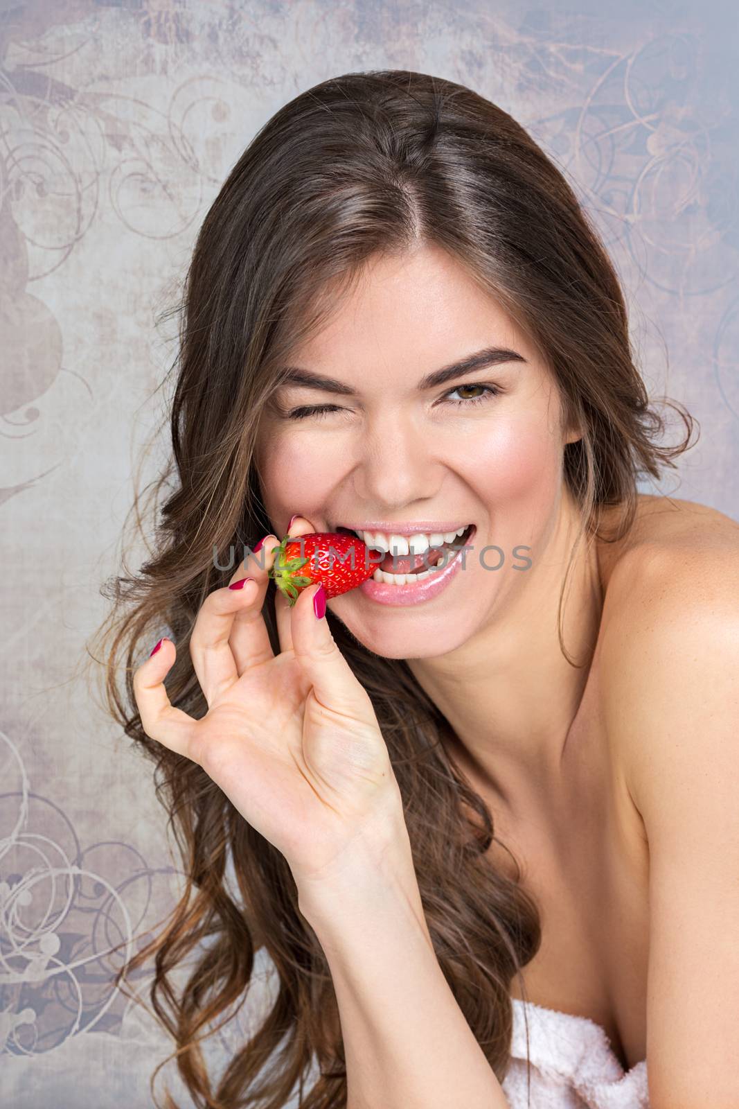 Studio portrait of a pretty girl with wavy fair hair and natural make-up eating strawberry