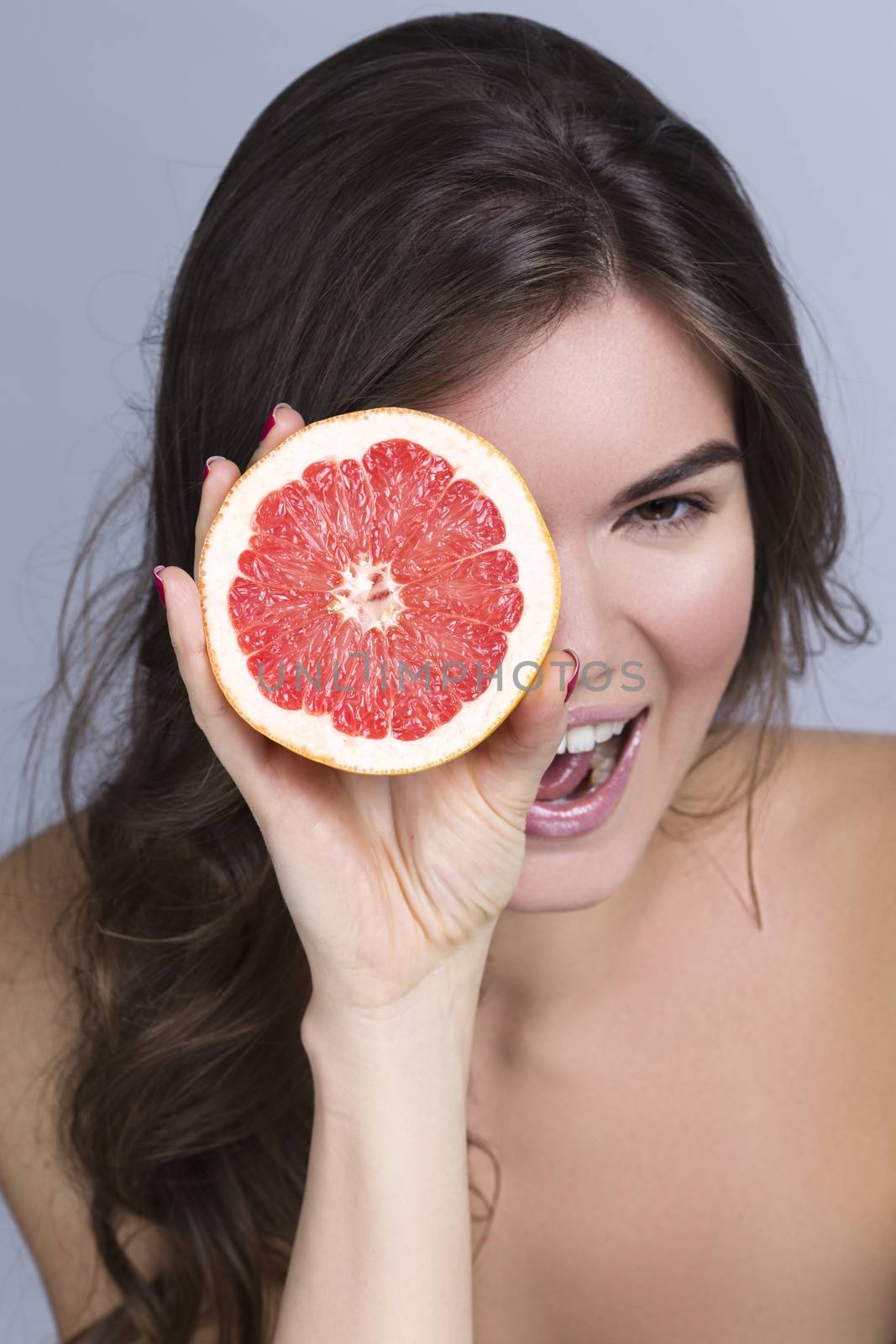 Young smiling woman looking through slice of grapefruit