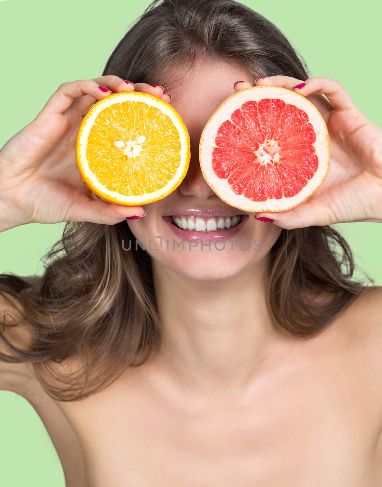 Smiling woman holding slices of orange and grapefruit in front of her eyes