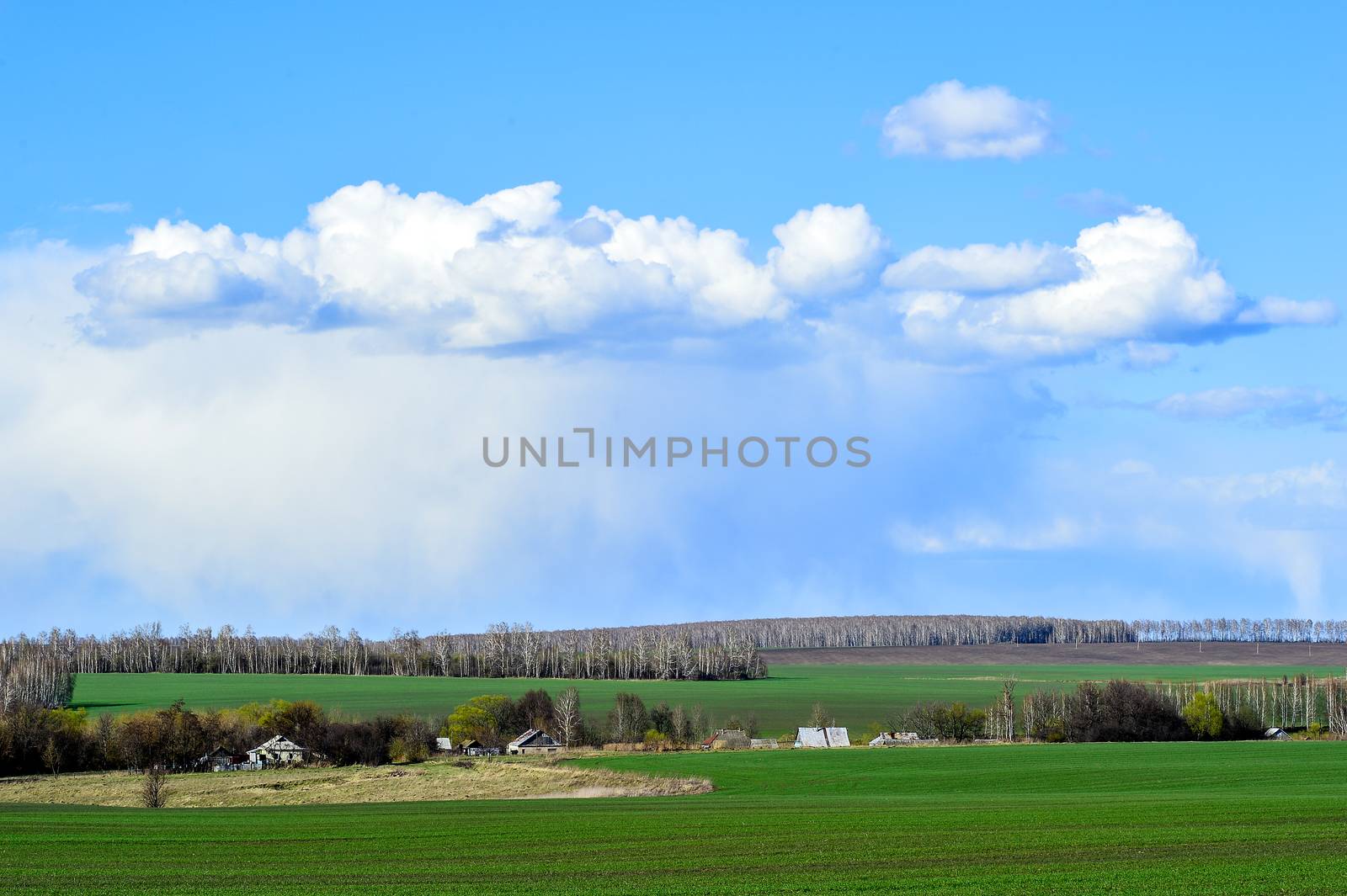Rural landscape with a green field, clouds and farm.