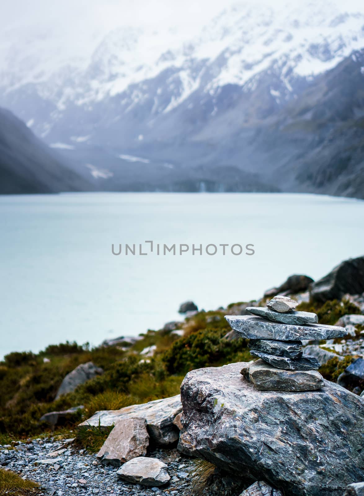 Rocks piled in a cairn in front of hooker lake in New Zealand. Tranquil scene with mountains in the background.