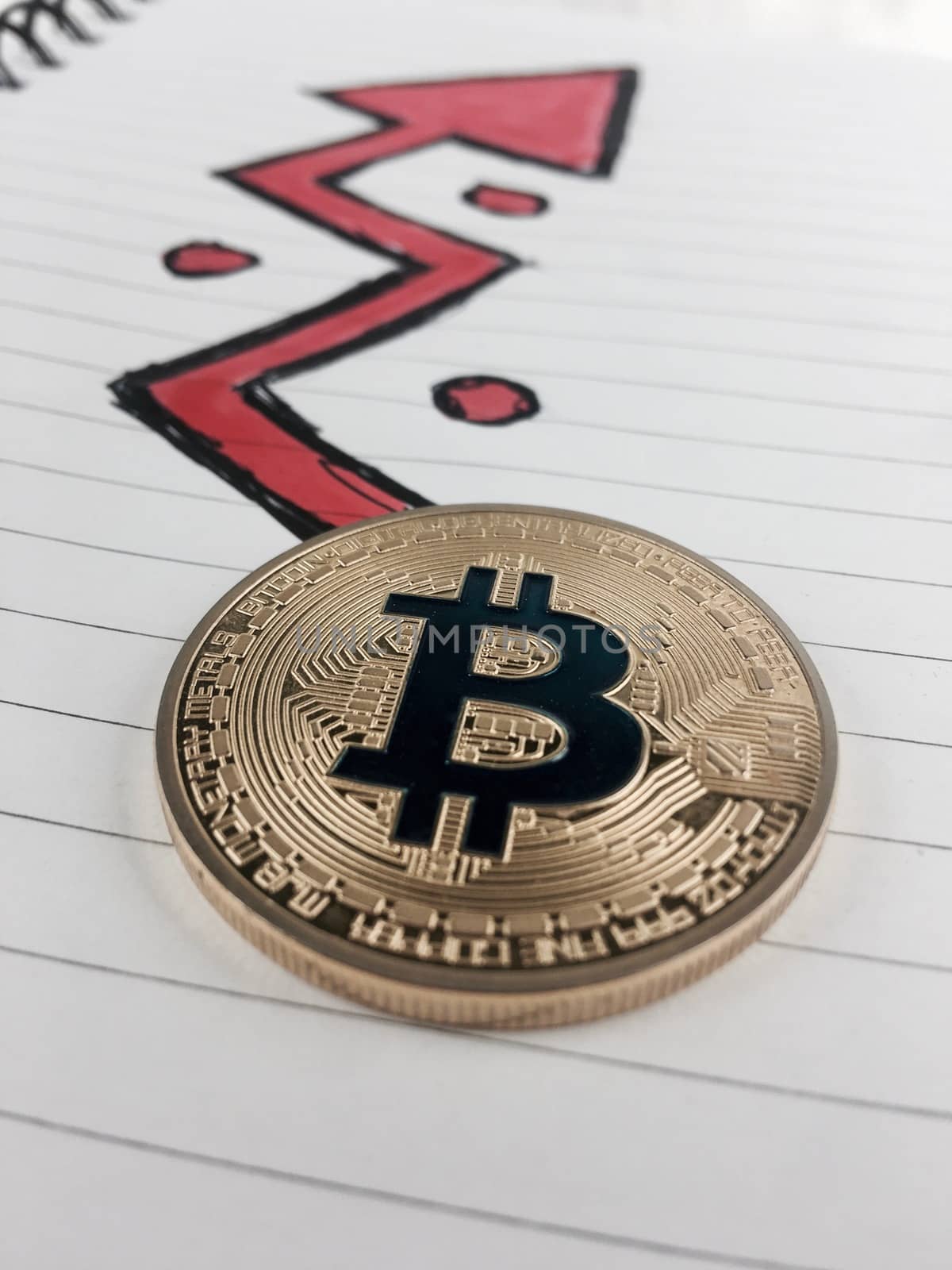 Cryptocurrency physical gold bitcoin coin and red arrow in notebook.