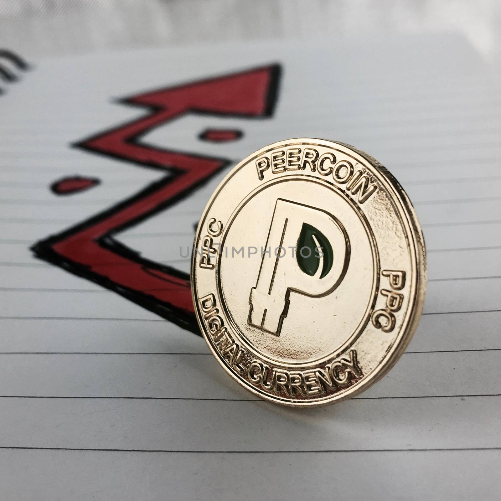 Digital currency physical gold peercoin coin and red arrow in notebook.