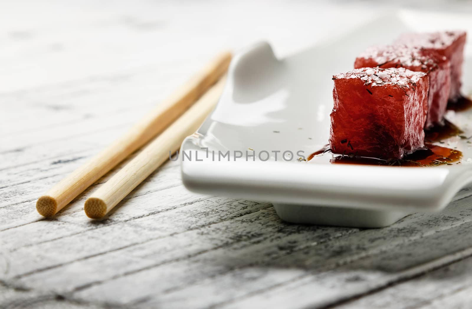 Tuna sashimi dipped in soy sauce,  thick salt and dill on old white wooden board with chopsticks. Raw fish in traditional Japanese style. Horizontal image.