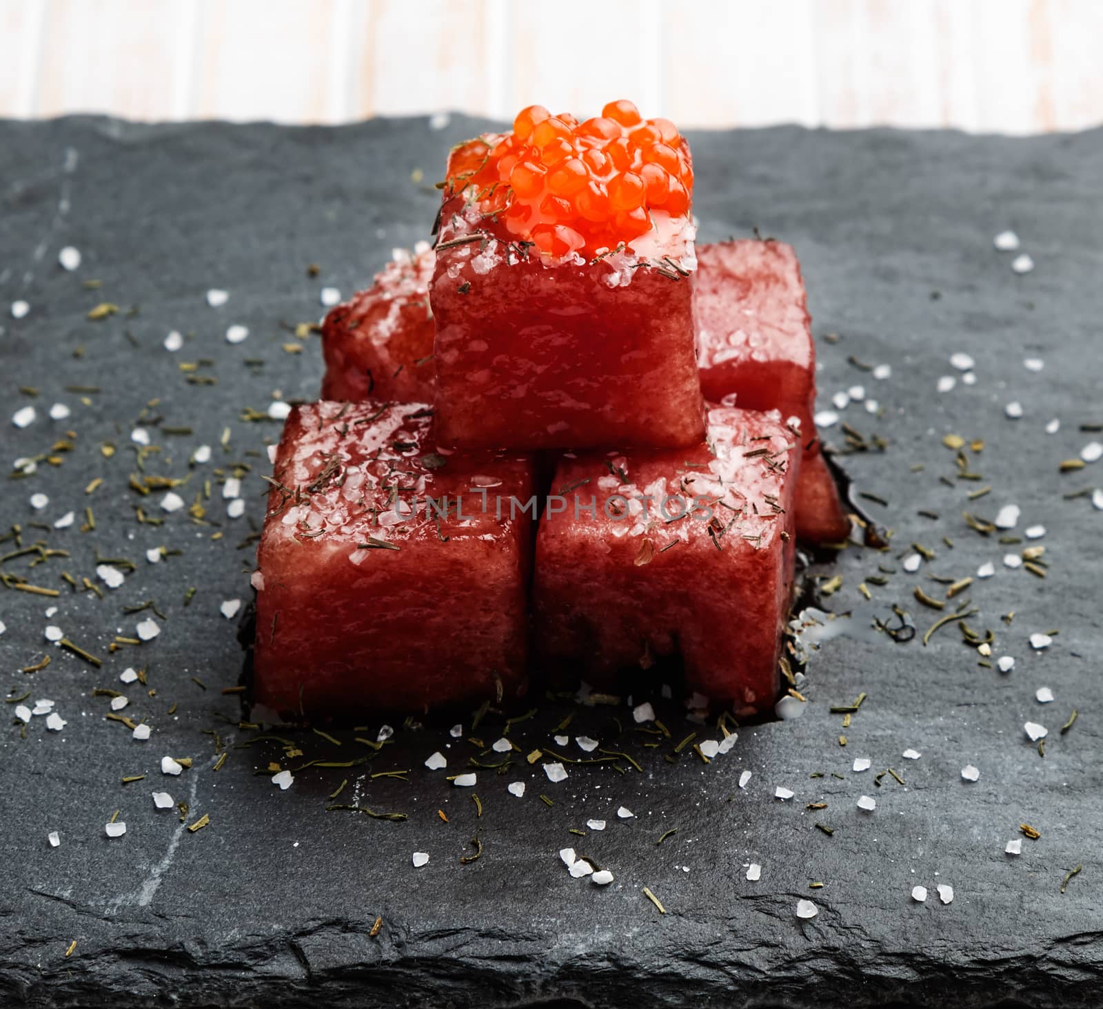 Tuna sashimi dipped in soy sauce with salmon roe, thick salt and dill on slate stone. Raw fish in traditional Japanese style. Horizontal image.