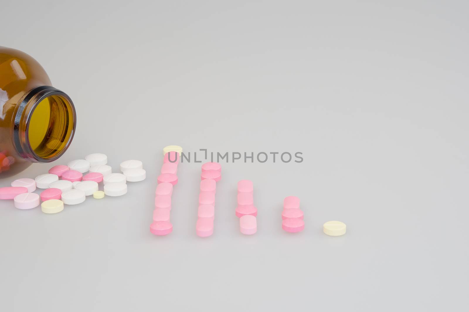 Colorful tablets place as bar graph and brown bottle with white background.