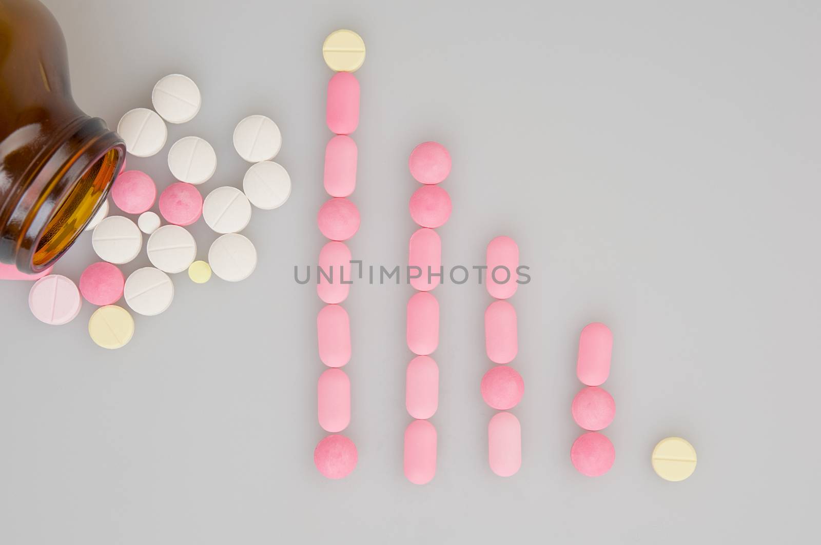 Colorful tablets place as bar graph and brown bottle on white background.
