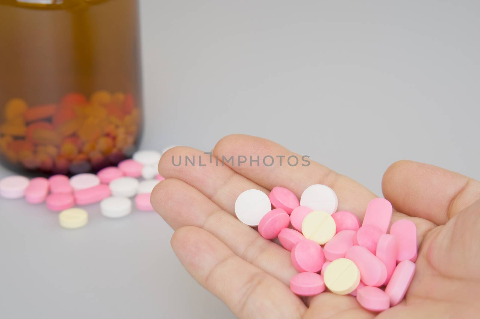 Hand of man holding colorful tablets have blur brown bottle place on white background.