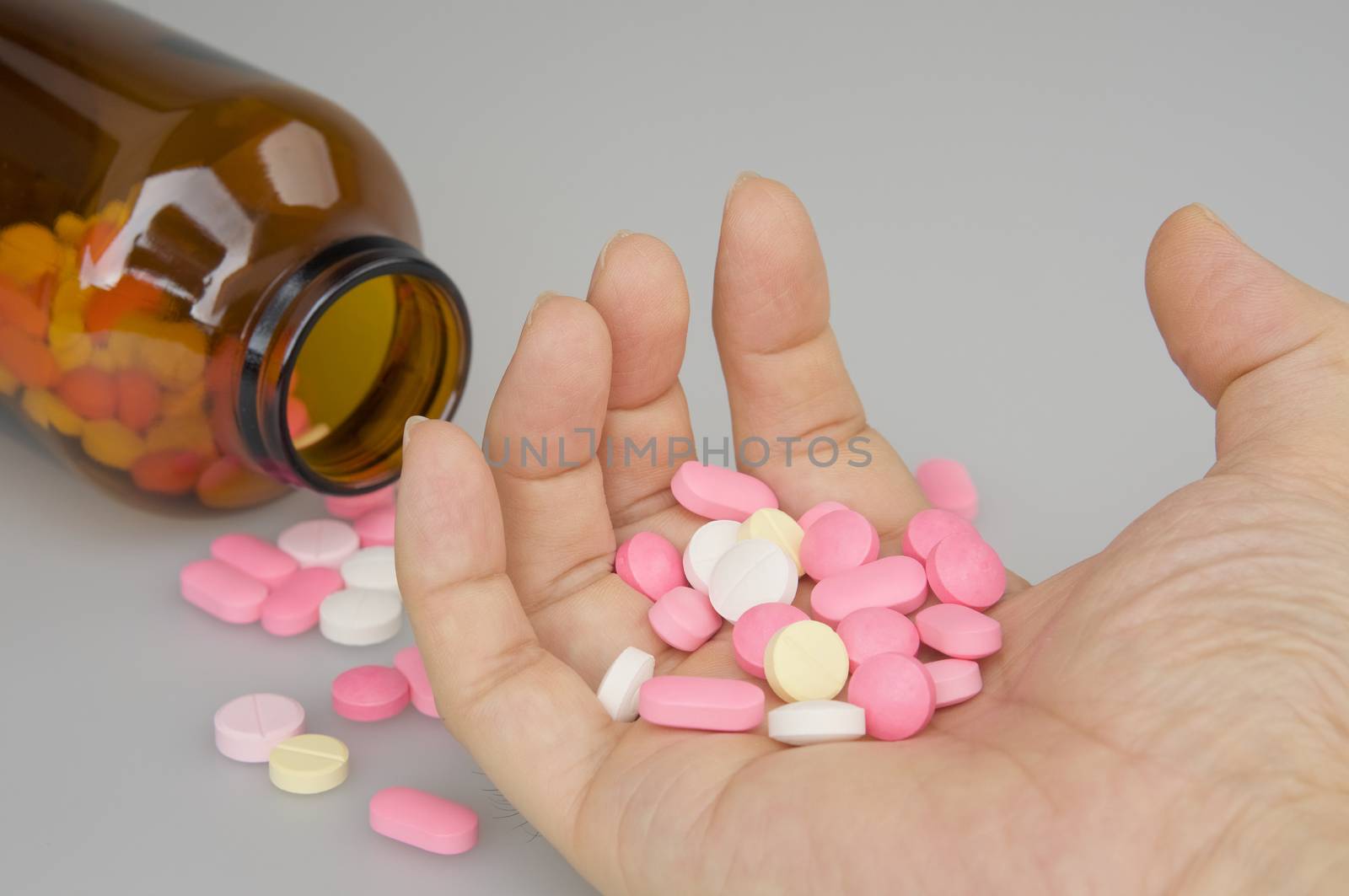 Contraction hand of man holding colorful tablets have blur brown bottle place on white background.