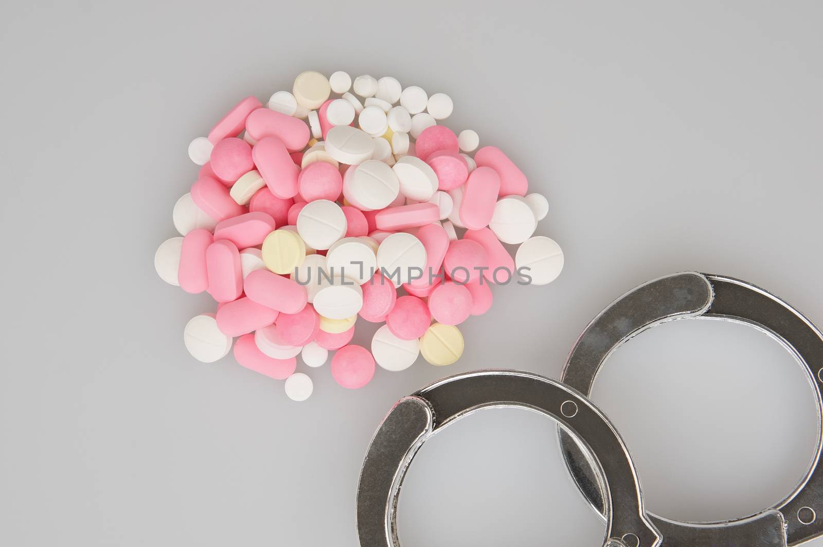 Silver handcuffs and stack of tablets place on white background.