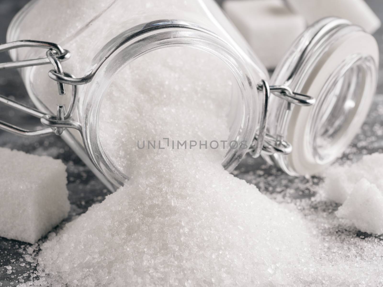 Close up view of white sugar on gray galvanized iron background. Granulated sugar in glass jar and sugar cubes. Sugar background. Copy space.