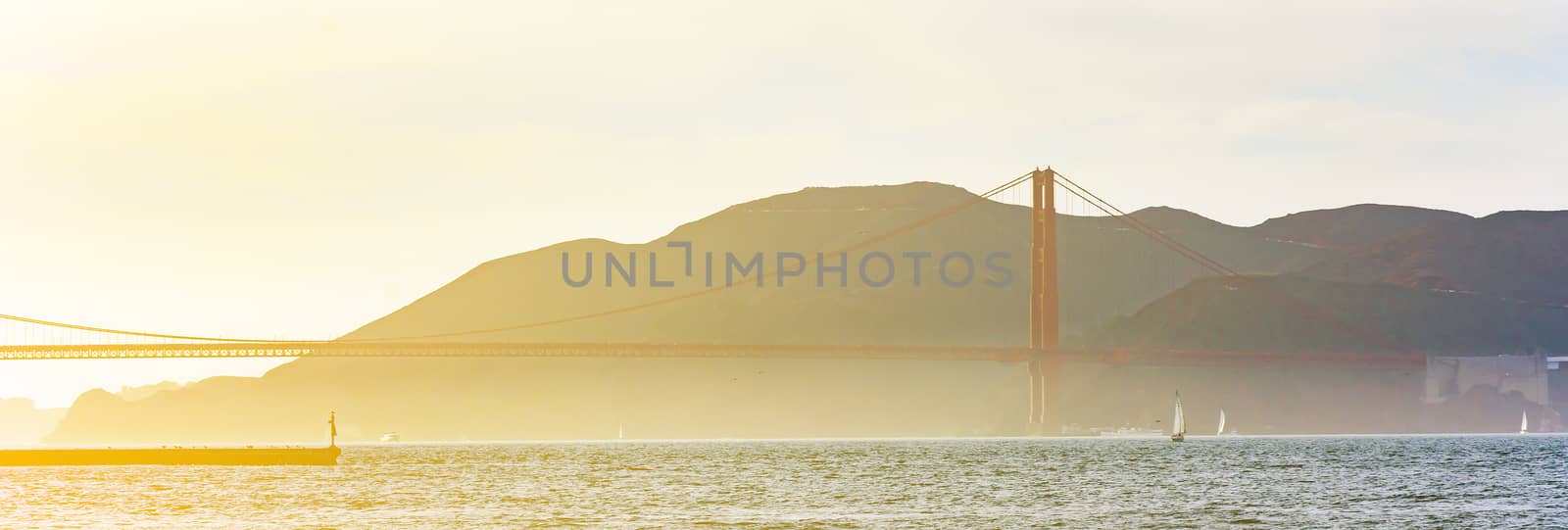 San Francisco bay area viewed from Pier 39 with foggy Golden Gate bridge in the distance in a bright sunset