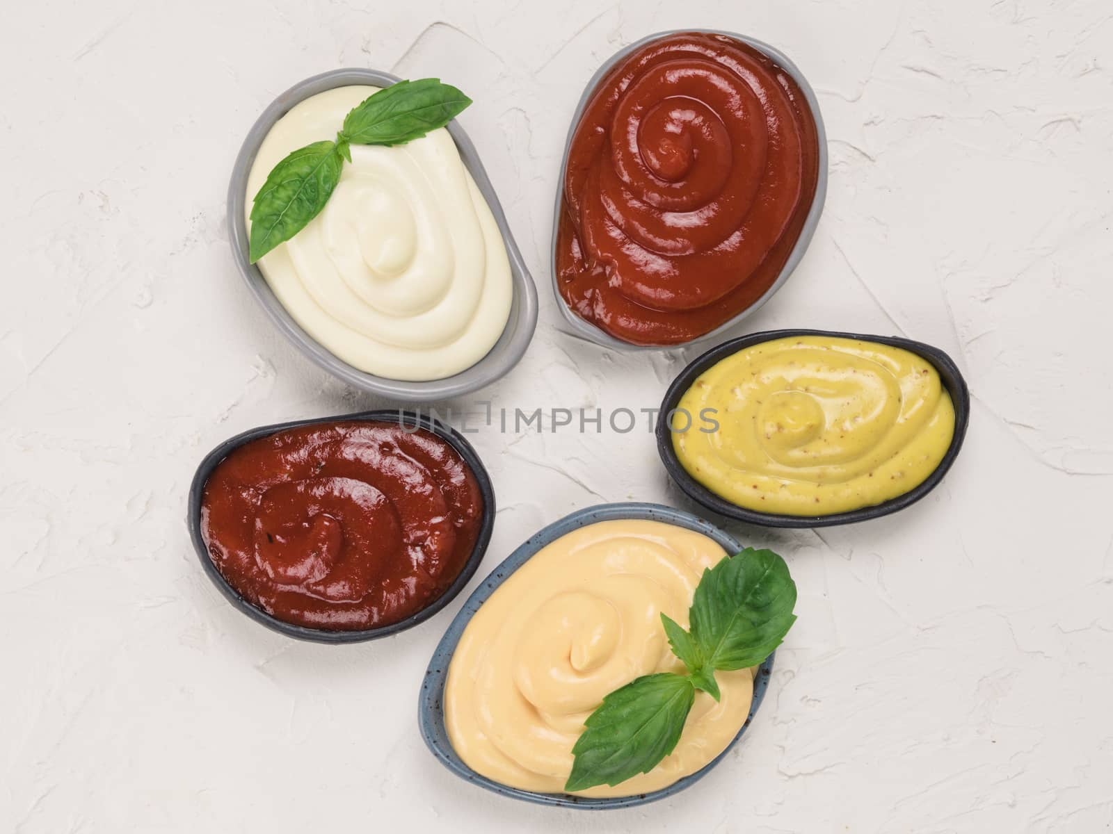 Top view of classic sauces set in trendy plates on white concrete background. Sauces set - salsa, mustard, ketchup, mayonnaise, cheese sauce, and basil for serve. Flat lay.