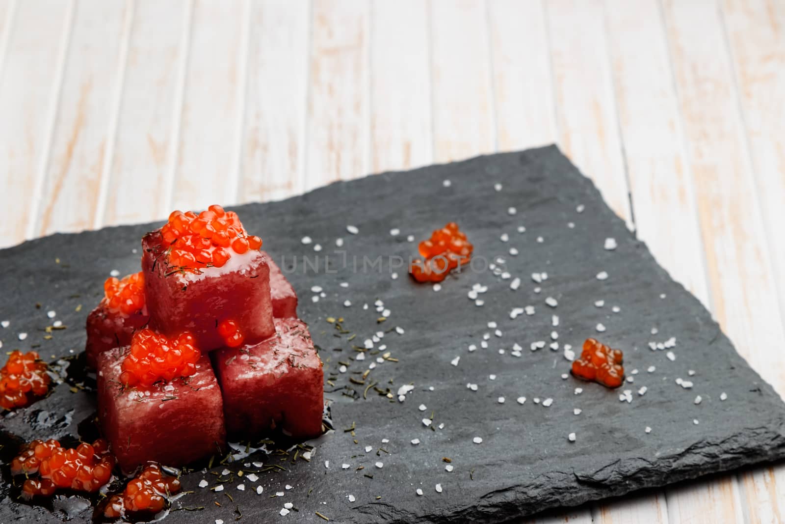 Tuna sashimi dipped in soy sauce with salmon roe, thick salt and dill on slate stone. Raw fish in traditional Japanese style. Horizontal image.