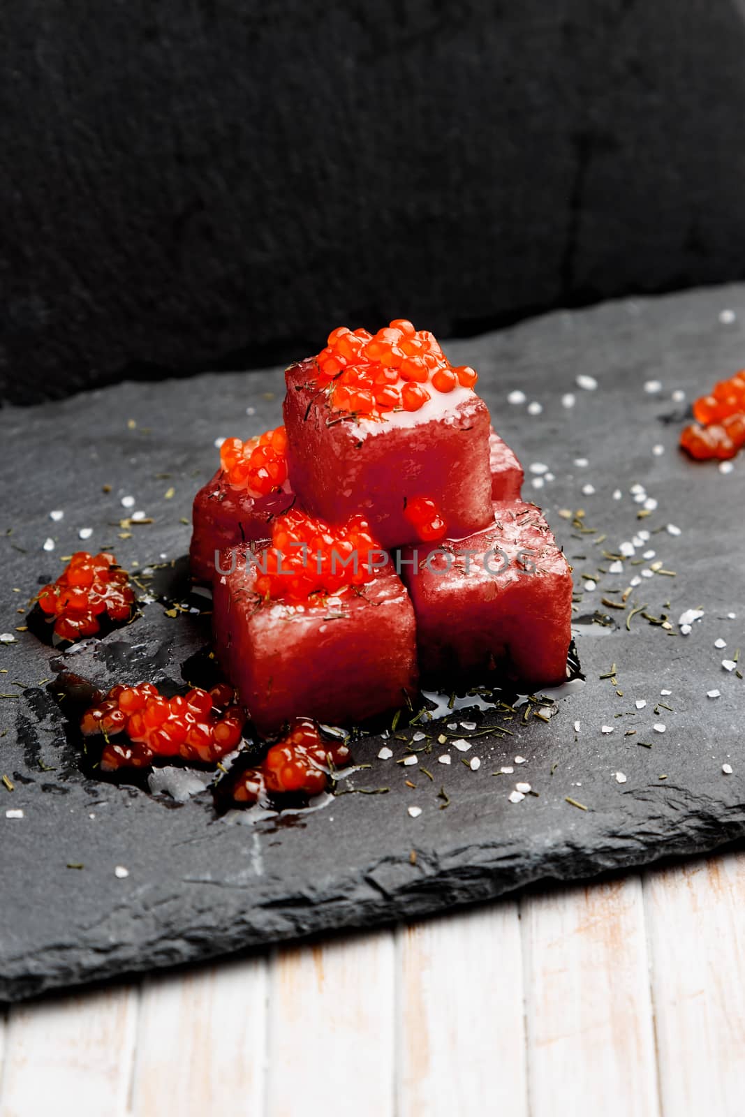Tuna sashimi dipped in soy sauce with salmon roe, thick salt and dill on slate stone. Raw fish in traditional Japanese style. Vertical image.