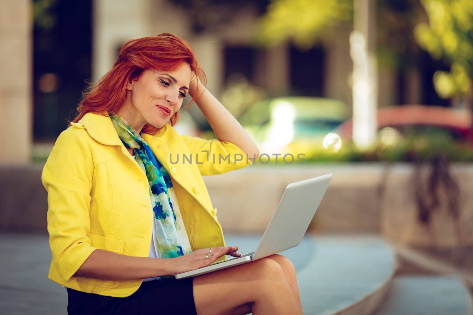 Smiling businesswoman sitting on stairs in office district and working at the laptop.