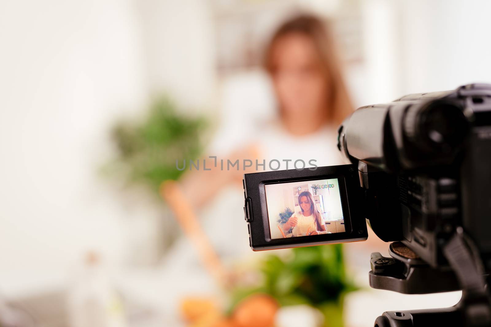 Beautiful young woman filming her blog broadcast about healthy food at the home. Selectiv focus. Focus on foreground, on camera.