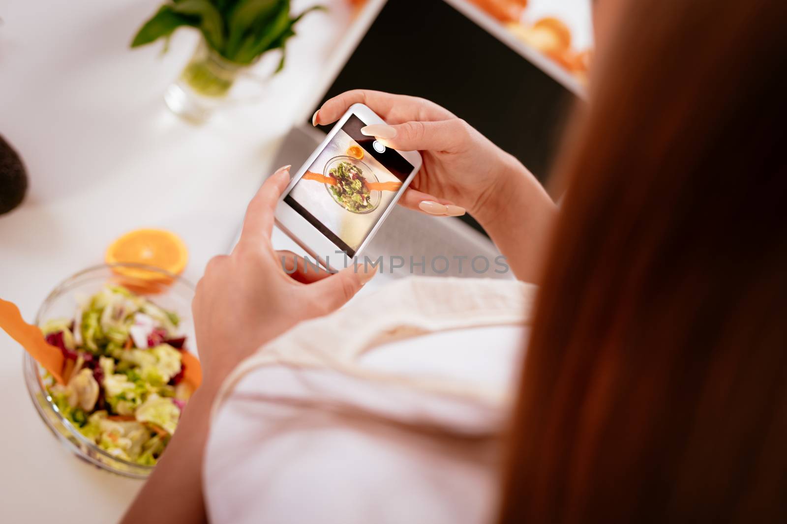 Close-up of a young woman taking photo of healthy salad with smartphone for her blog. Rear view. Selective focus.