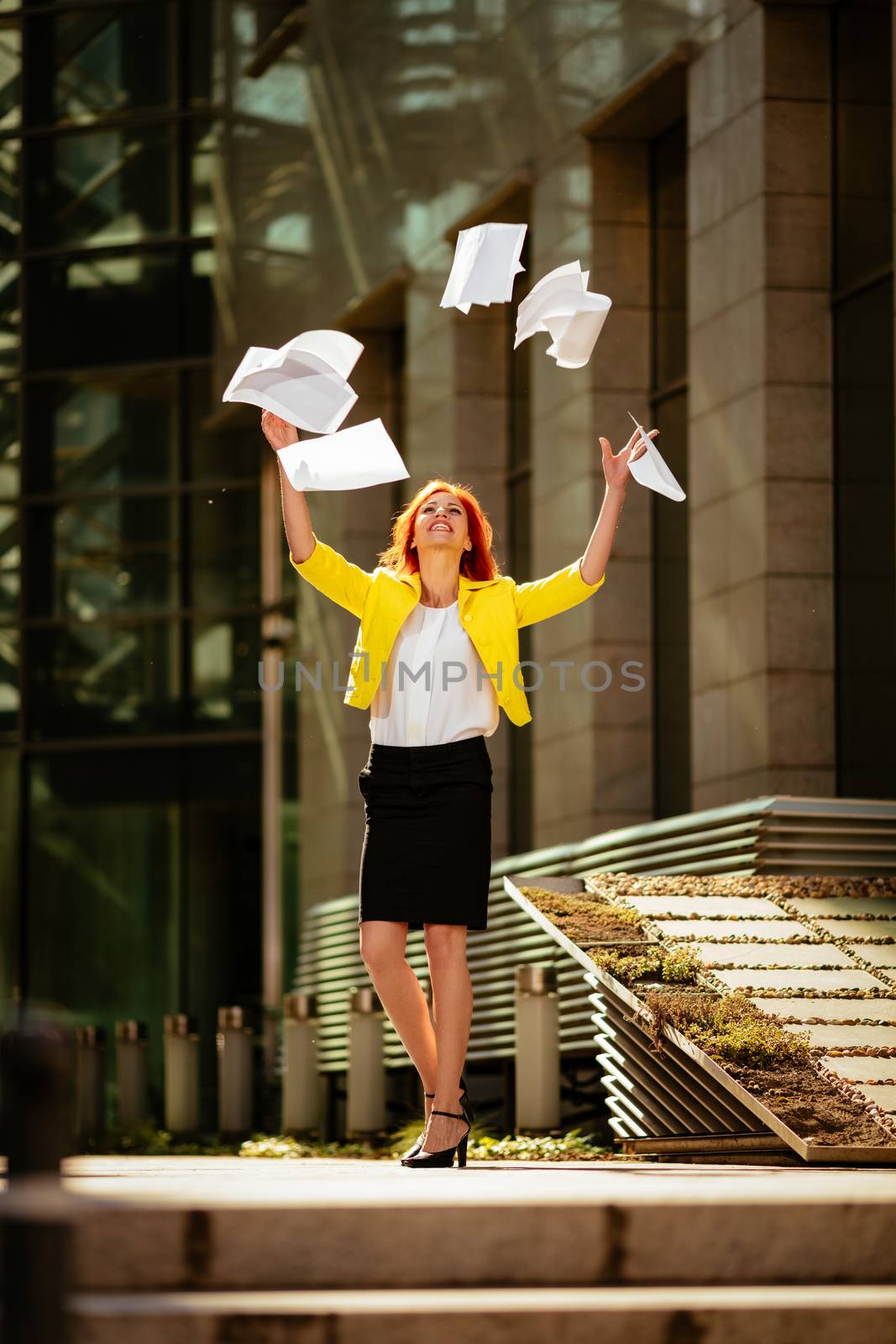 Happiness businesswoman celebrating success and throwing papers in the air in office district. 