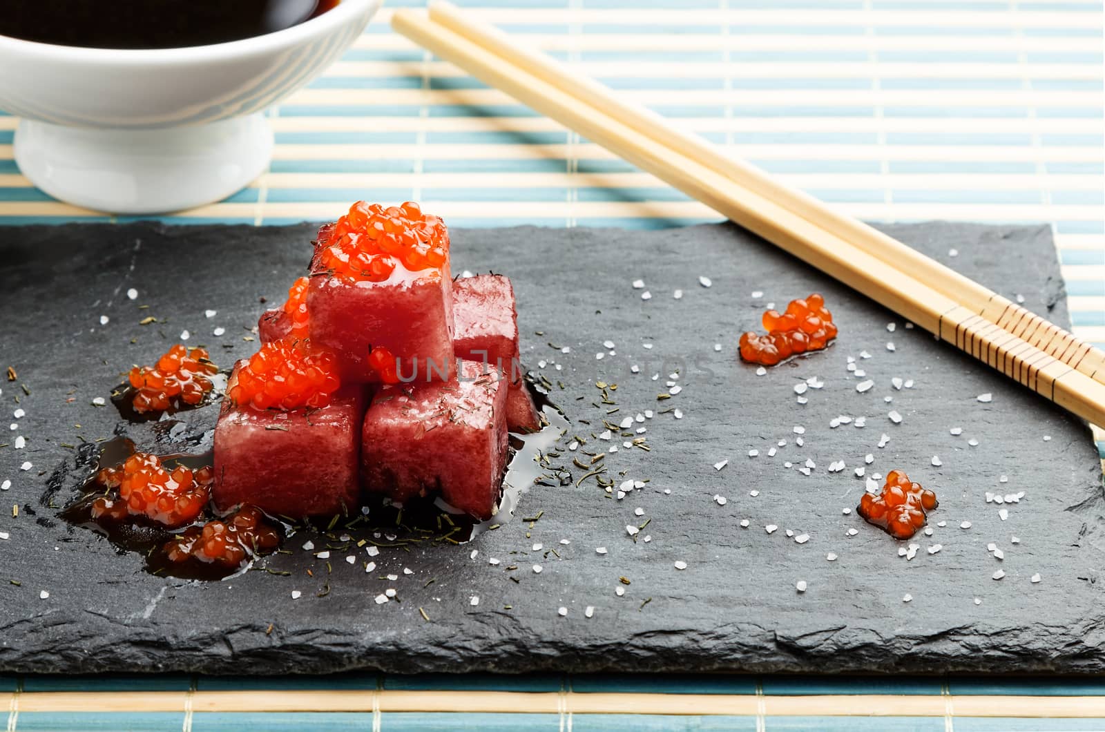 Tuna sashimi dipped in soy sauce with salmon roe, thick salt and dill on slate stone with chopsticks and bowl with soy. Raw fish in traditional Japanese style. Horizontal image.