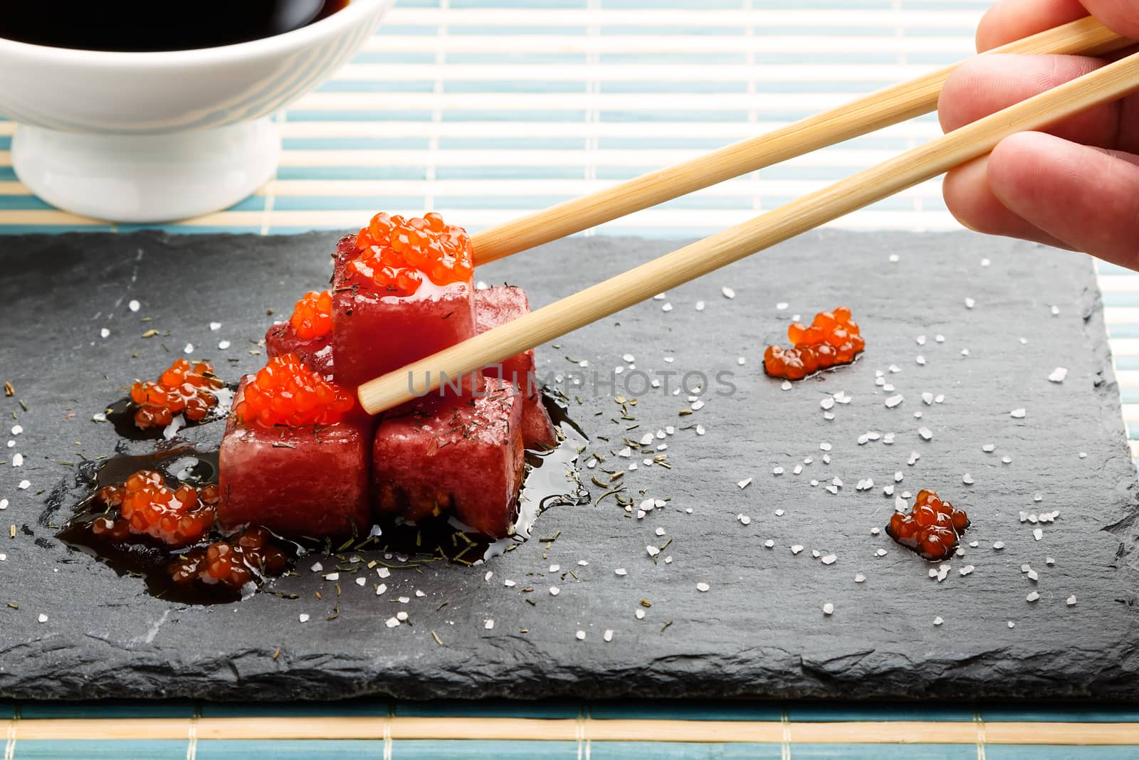 Tuna sashimi dipped in soy sauce with salmon roe, thick salt and dill on slate stone with chopsticks and bowl with soy. Raw fish in traditional Japanese style. Horizontal image.