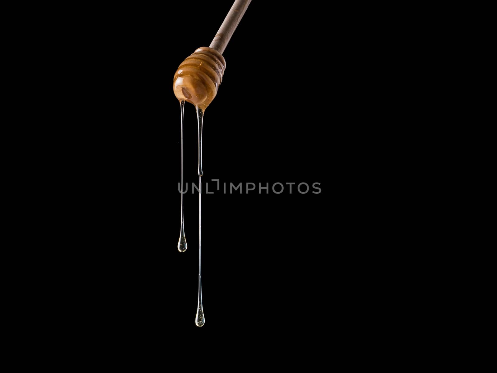 Organic honey flows from dipper. Isolated on black. Copy space. Honey stick with flowing honey