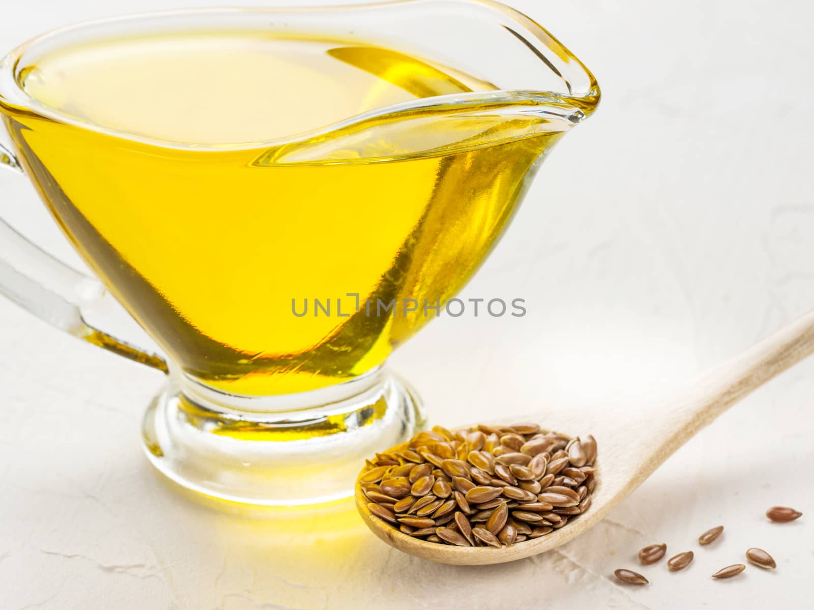 Brown flax seeds in spoon and flaxseed oil in glass jug on trendy textured white concrete background. Flax oil is rich in omega-3 fatty acid.