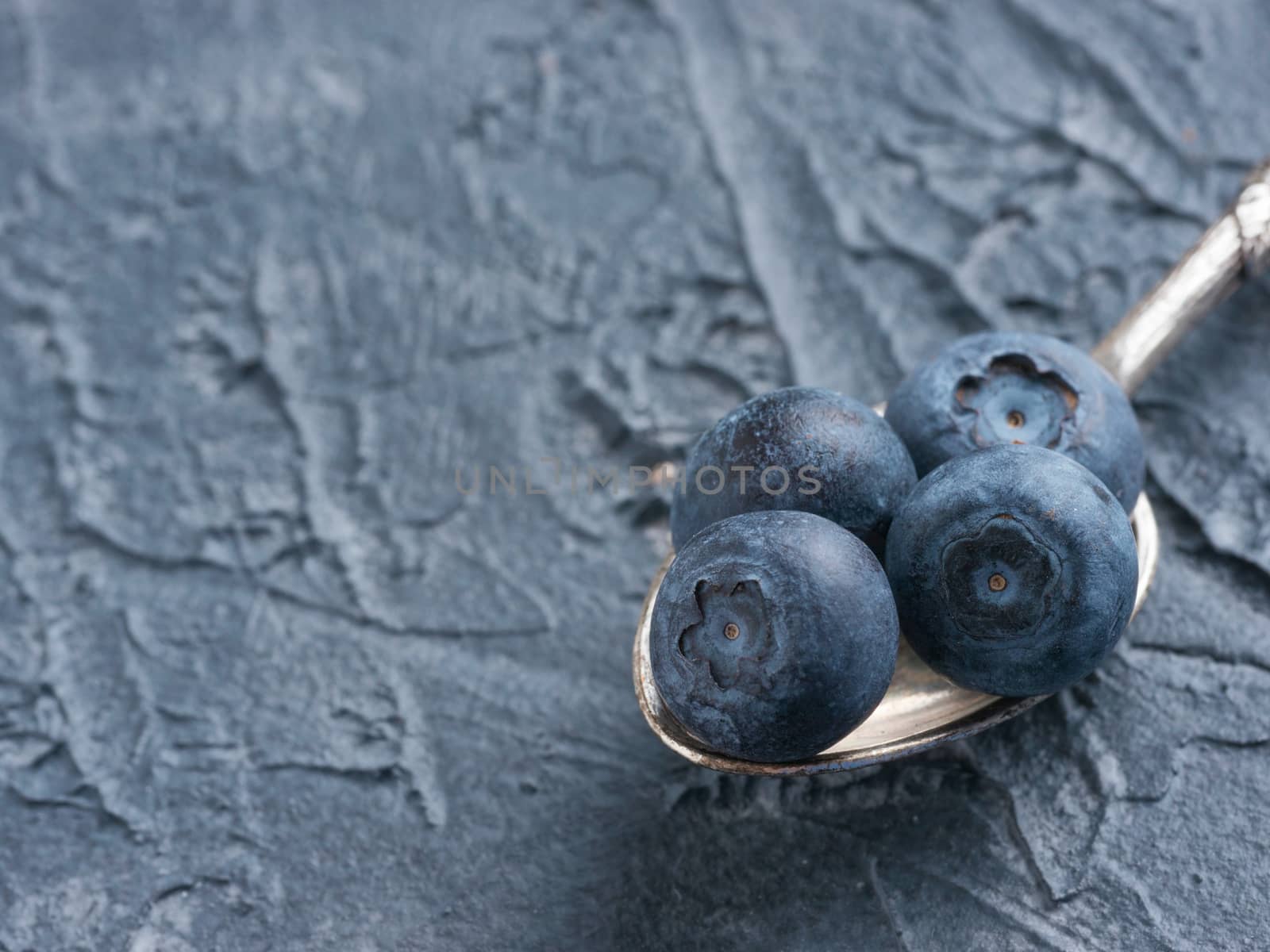 Freshly picked blueberries in spoon closeup. Ripe and juicy fresh blueberries on textured concrete background. Bilberry on dark background with copyspace. Blueberry antioxidant. Healthy eating concept