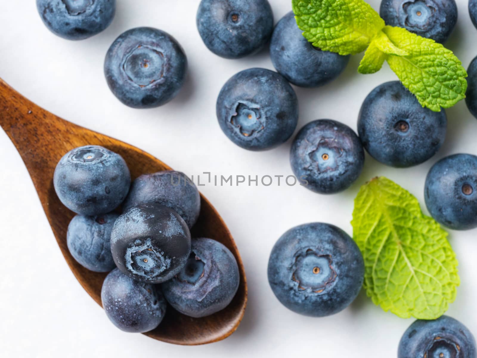 Freshly picked blueberries in wooden spoon closeup. Ripe and juicy fresh blueberries with green mint leaves on white background. Bilberry antioxidant. Healthy eating concept