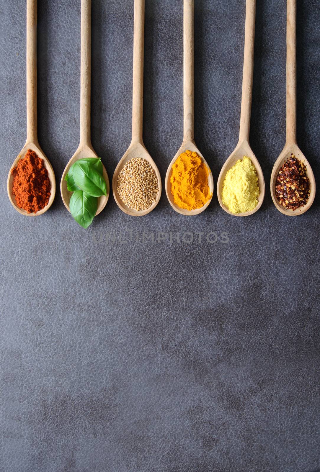 Various fresh herbs and spices in wooden spoons on a kitchen worktop background