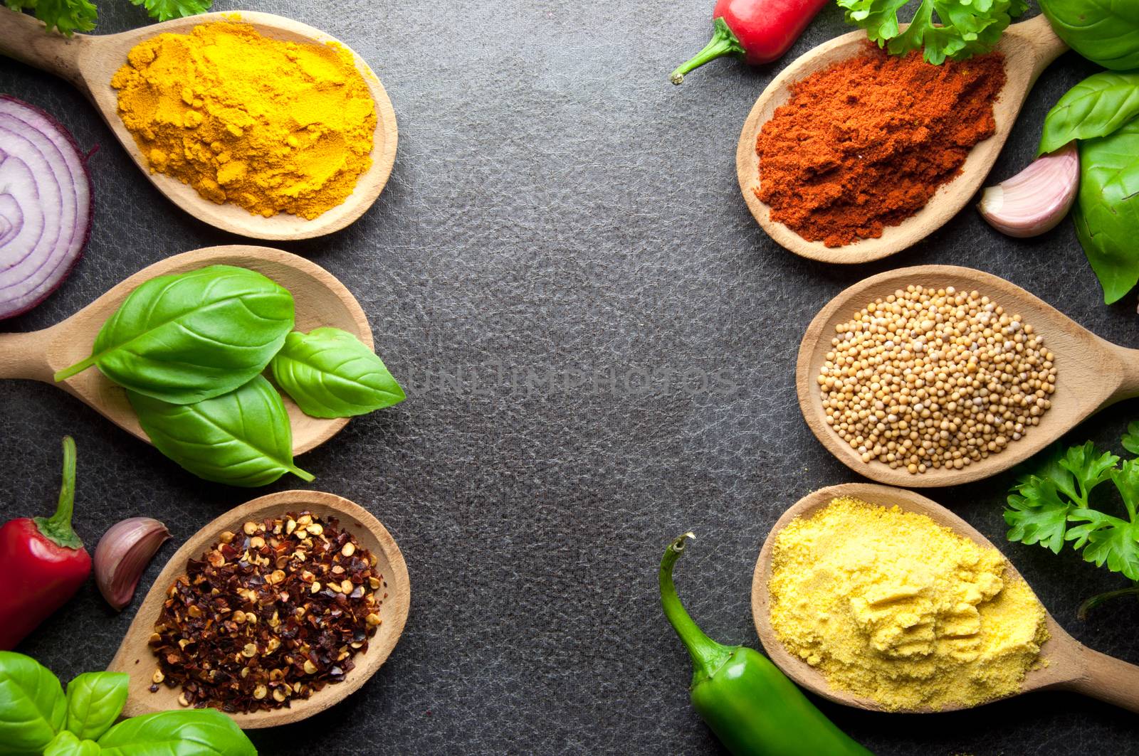 Fresh cooking ingredients including herbs and spices in wooden spoons on a kitchen worktop background