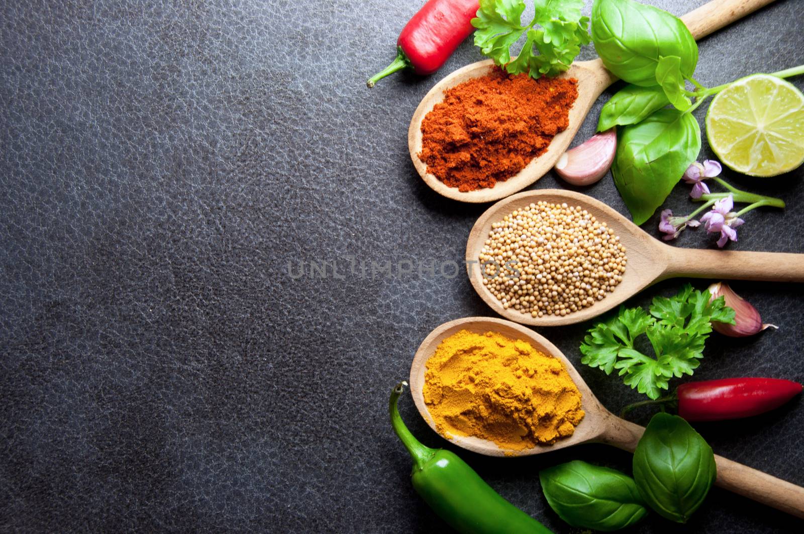 Fresh herbs and spices in wooden spoons kitchen worktop background