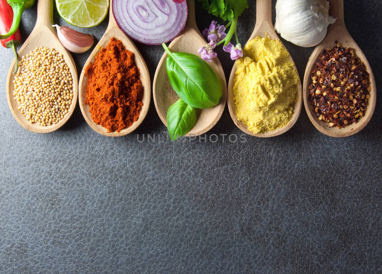 Fresh herbs and spices in wooden spoons kitchen worktop background 