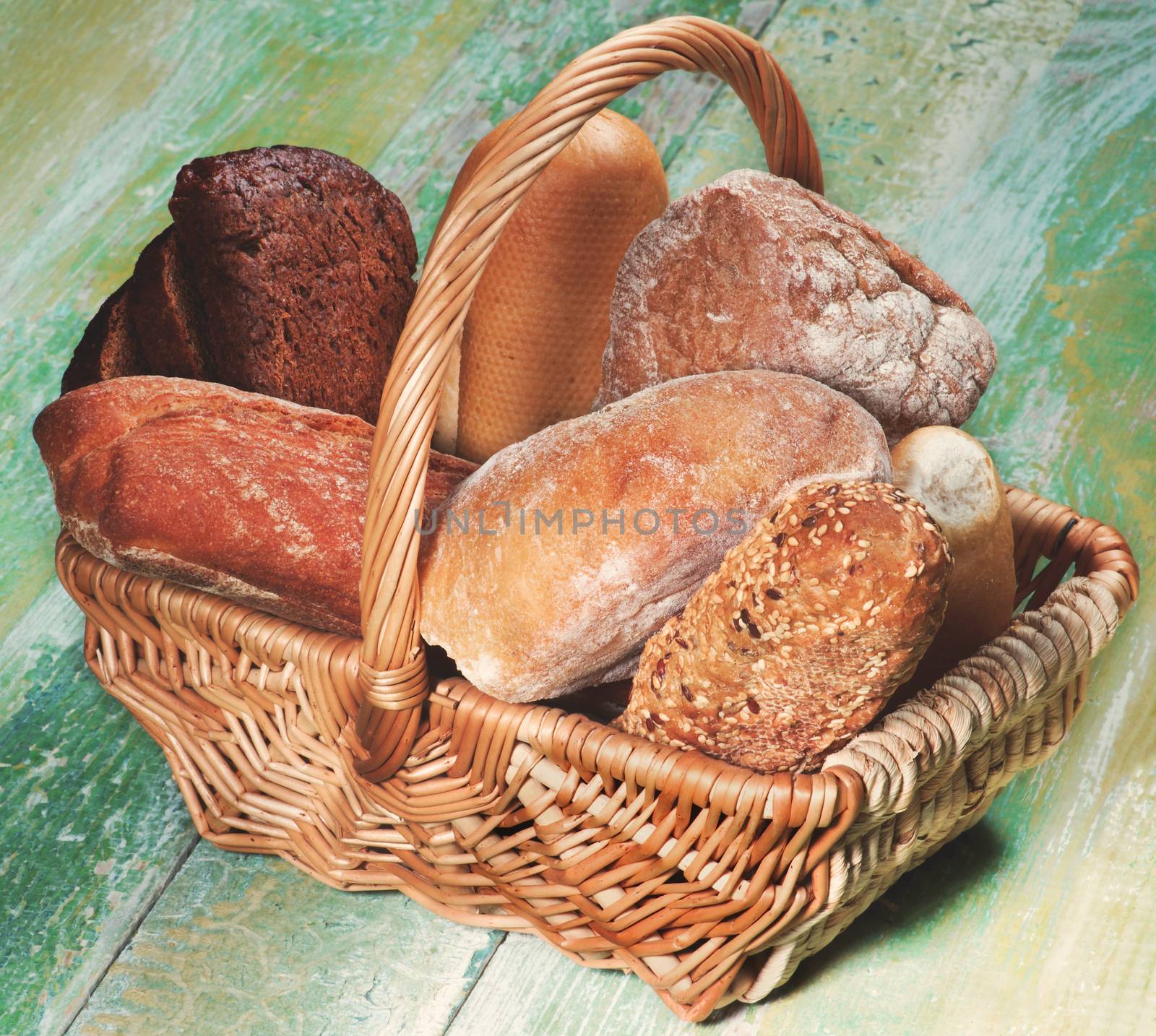 Various Buns, Baguette, Rye and Whole Wheat Bread in Wicker Basket closeup on Green Wooden background