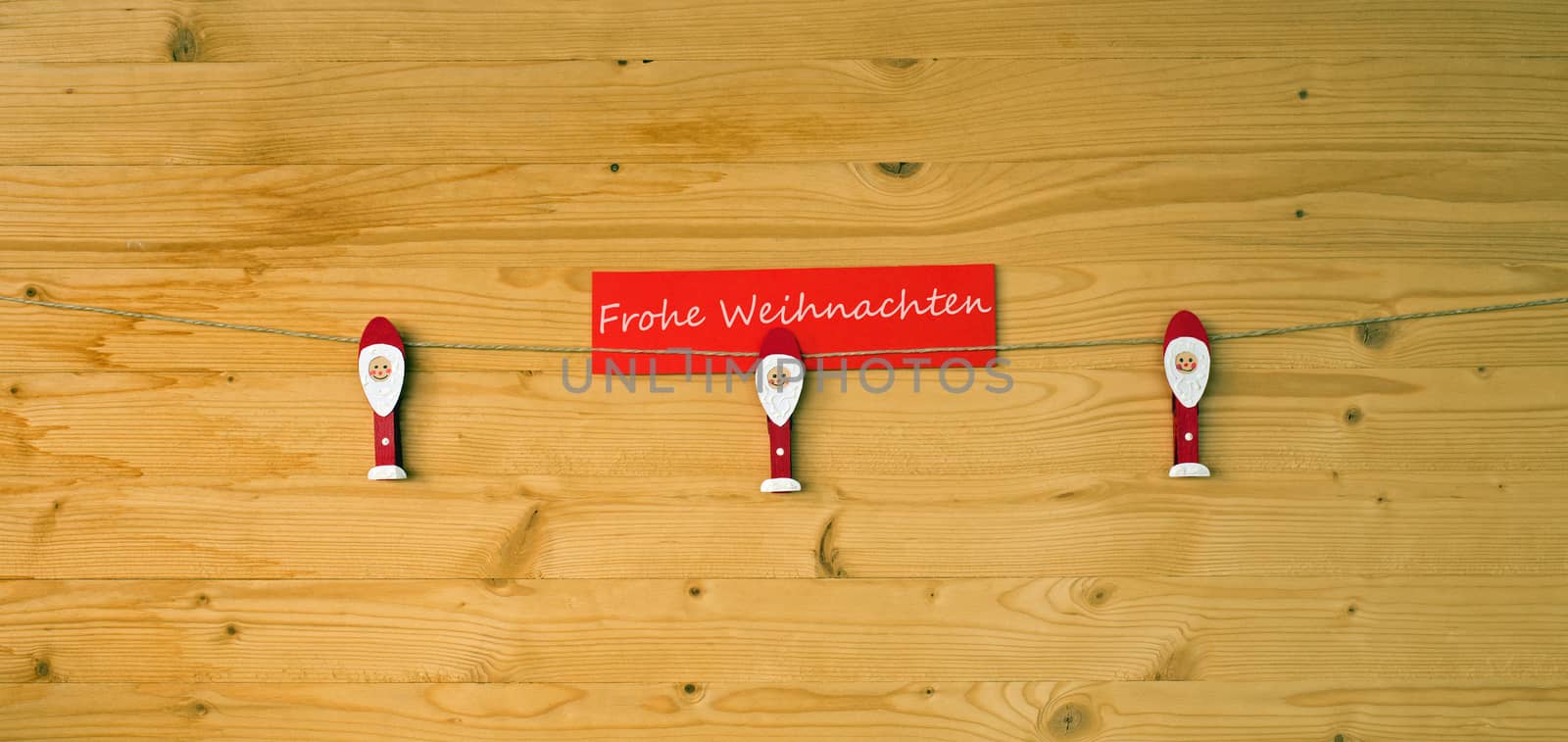 Three christmas men with clothes pegs on a cord on wood and german text for merry christmas