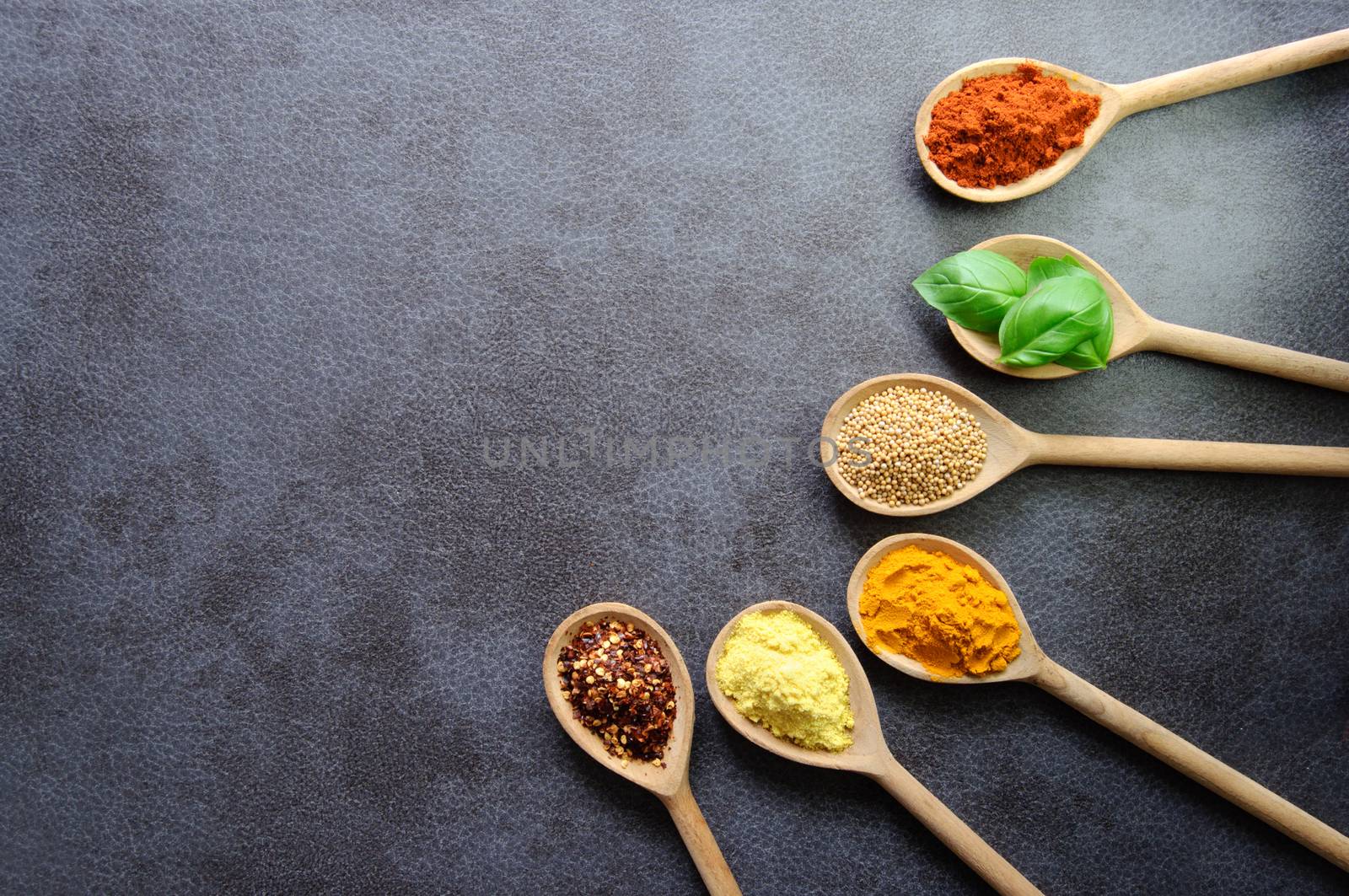 Wooden spoons with various fresh herbs and spices on a kitchen worktop background