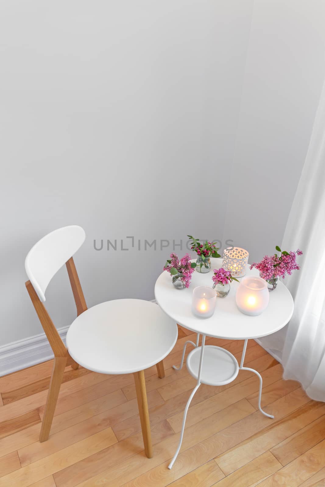 Elegant home interior with white chair and table, decorated with candle lights and spring flowers.