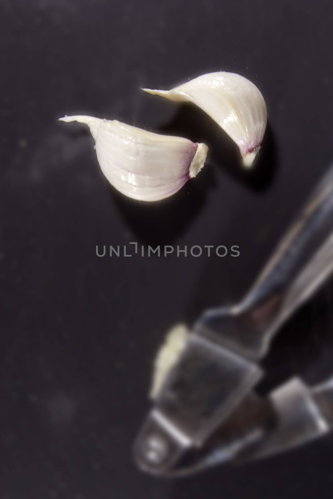 Garlic press and cloves of garlic, lying on a background of a stone board