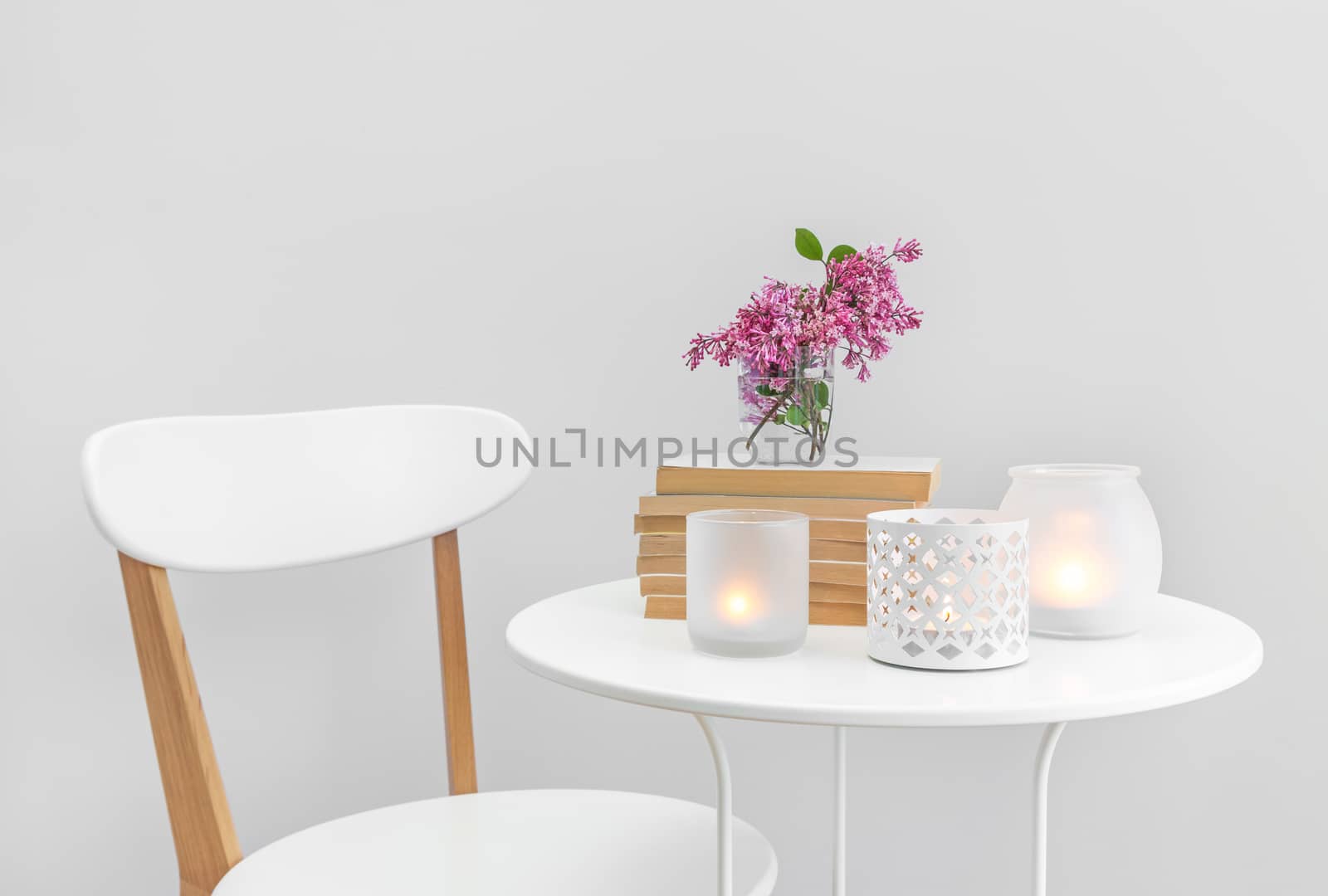 Candle lights, books and flowers on a white table by anikasalsera