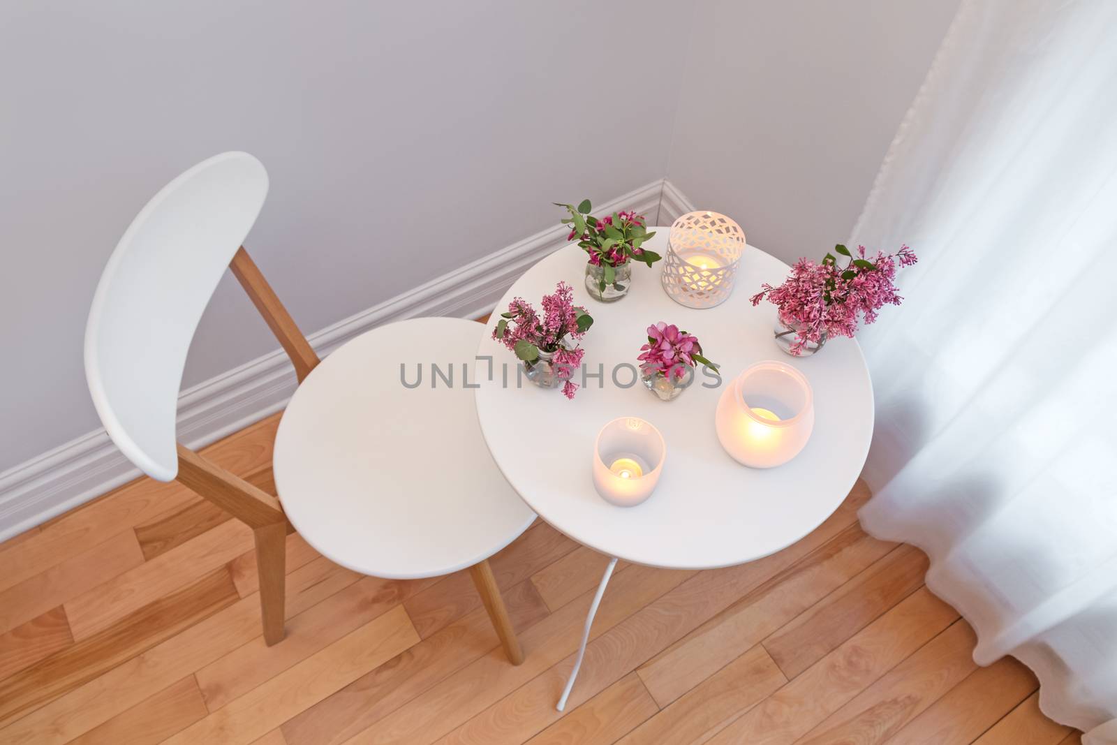 Cozy home interior with white chair and table, decorated with candle lights and spring flowers.