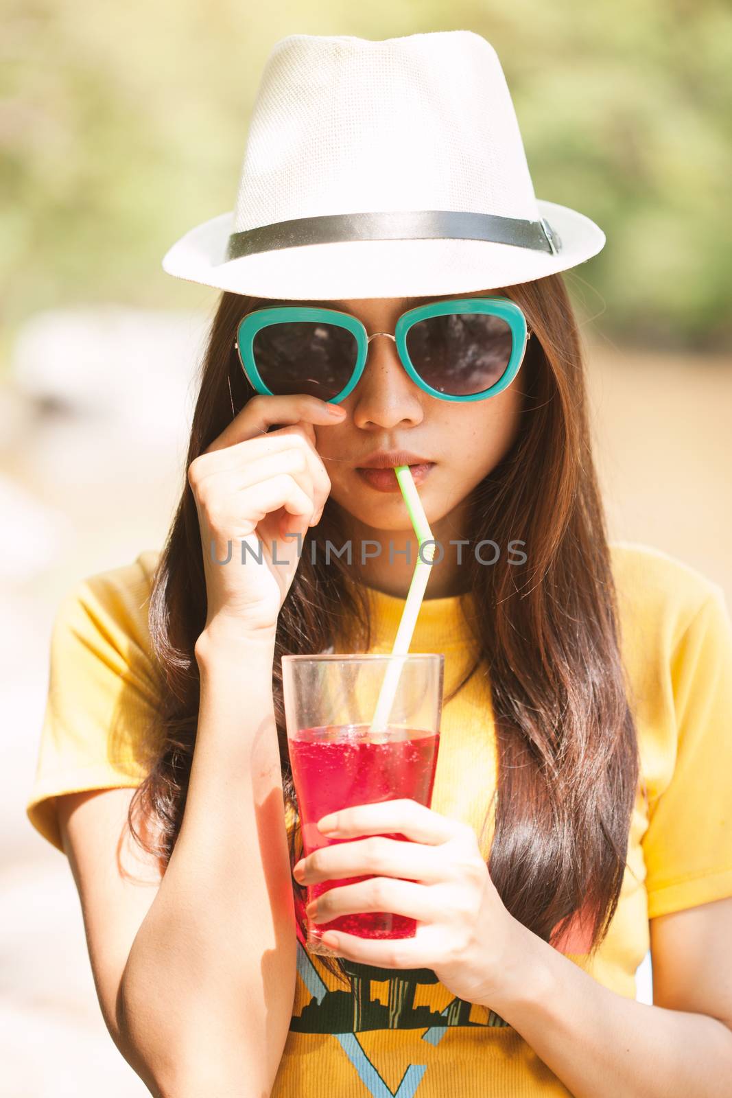 Woman drinking iced drinks outdoors with sand by the sea.