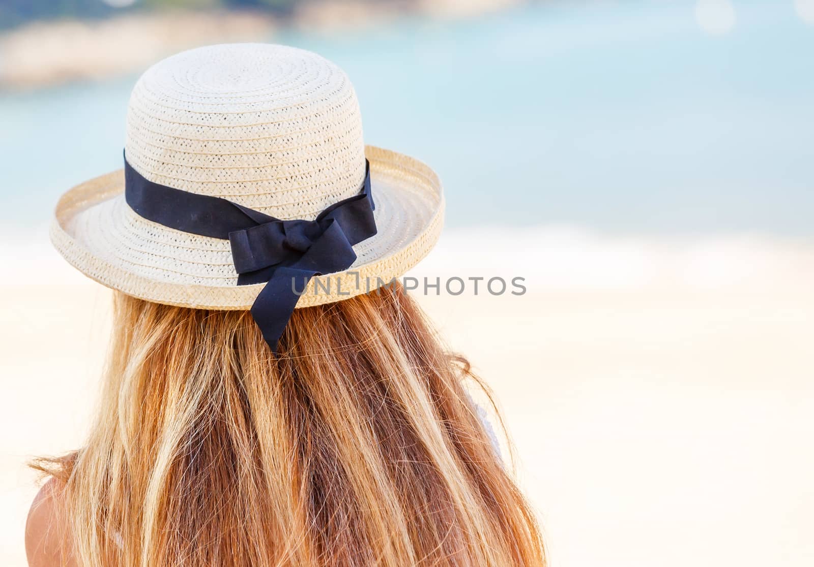 Back view of young woman with a straw hat on beach background by pixinoo