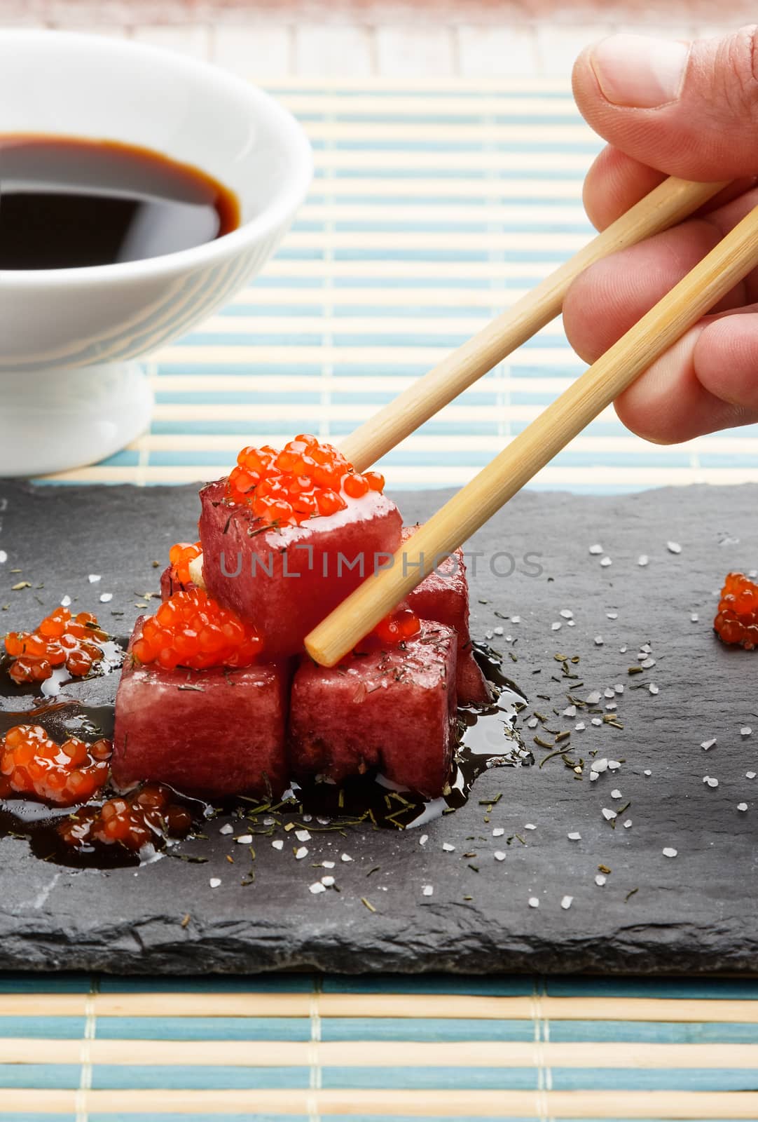 Tuna sashimi dipped in soy sauce with salmon roe, thick salt and dill on slate stone with chopsticks and bowl with soy. Raw fish in traditional Japanese style. Vertical image.