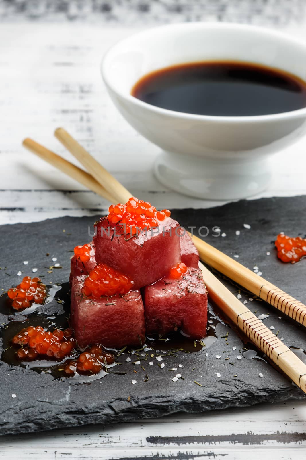 Tuna sashimi dipped in soy sauce with salmon roe, thick salt and dill on slate stone with chopsticks and bowl with soy. Raw fish in traditional Japanese style. Vertical image.