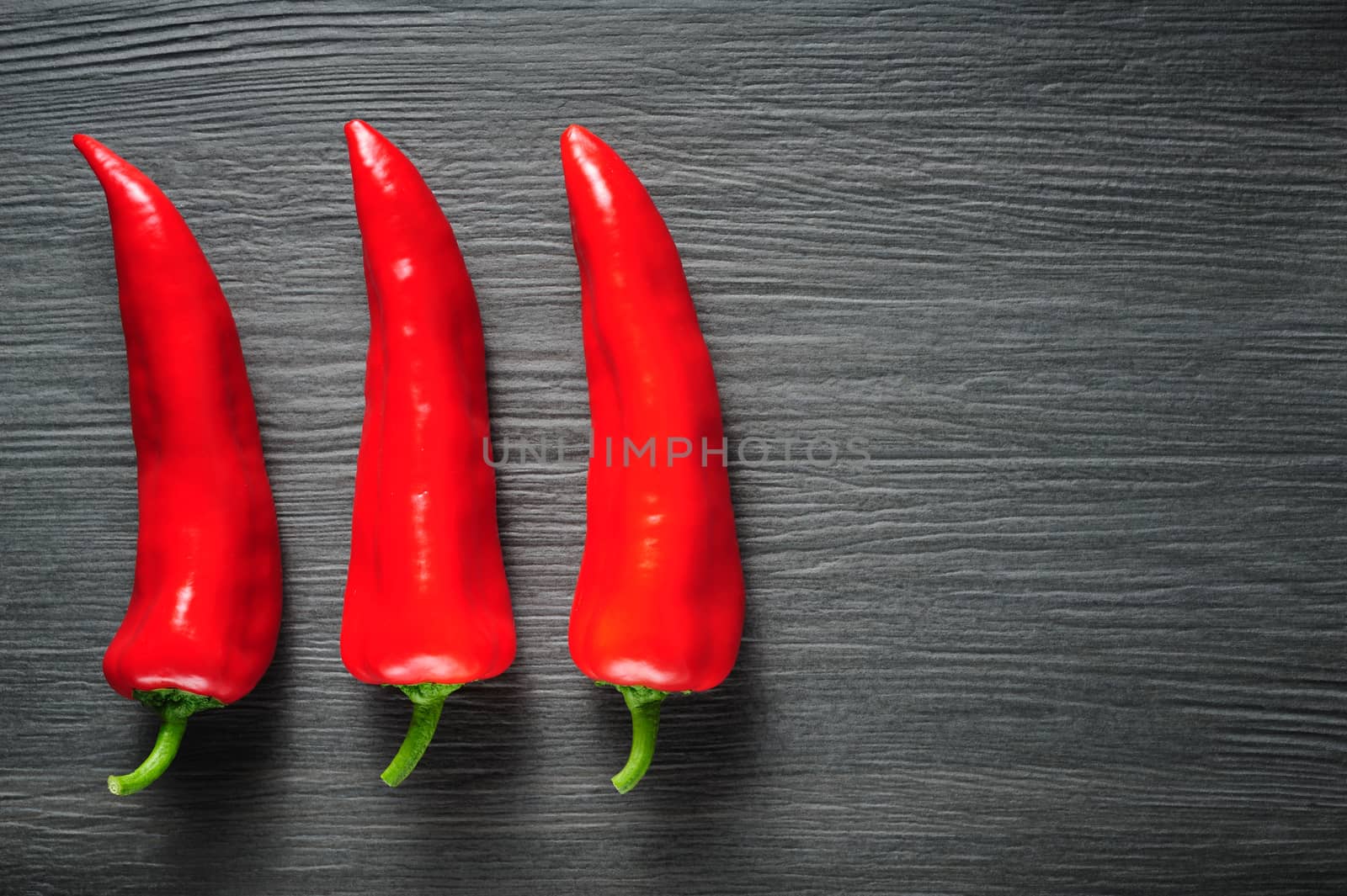 Three ripe sweet red Kapia peppers on dark shale stone background, copy space