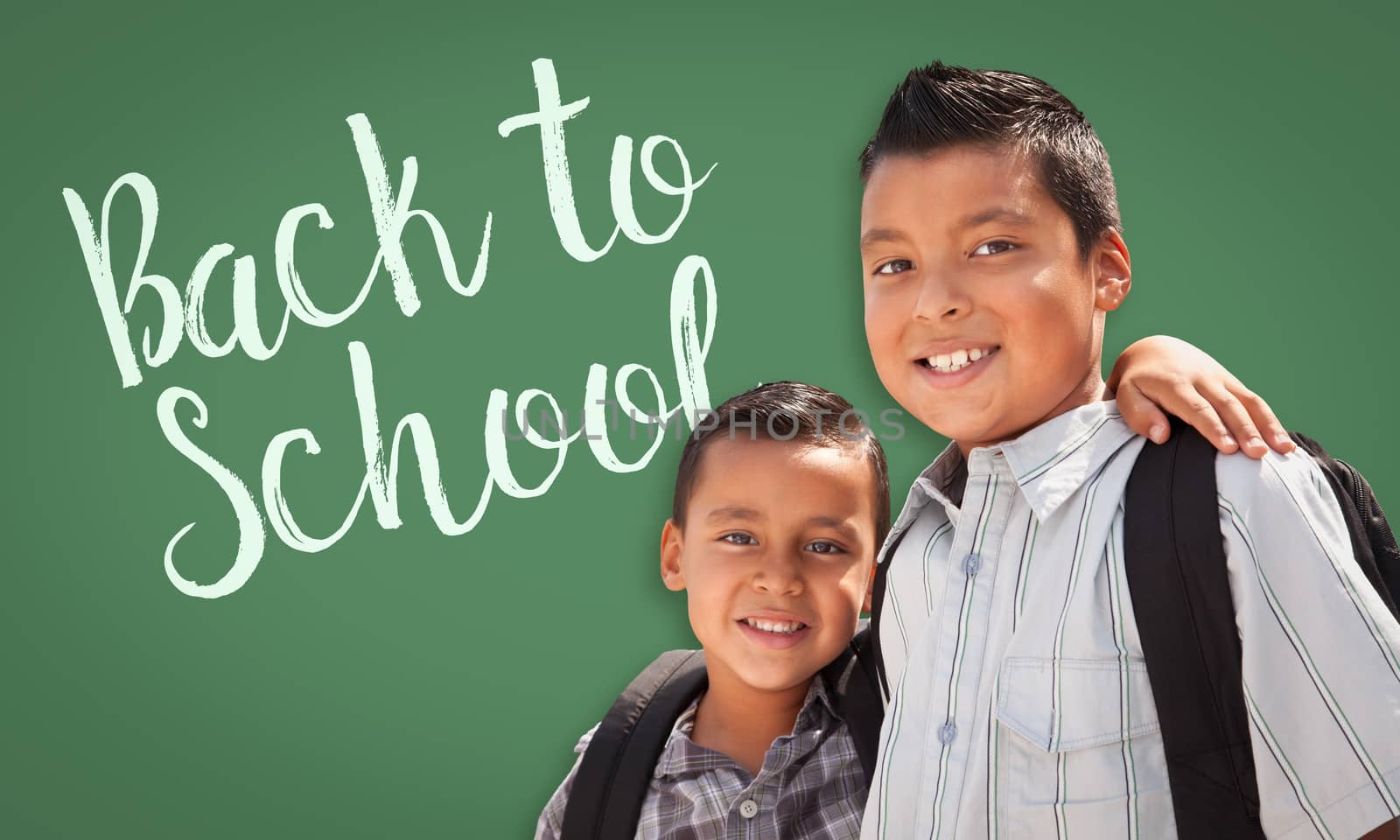 Cute Hispanic Boys Wearing Backpacks In Front of Back To School Written On Chalk Board.