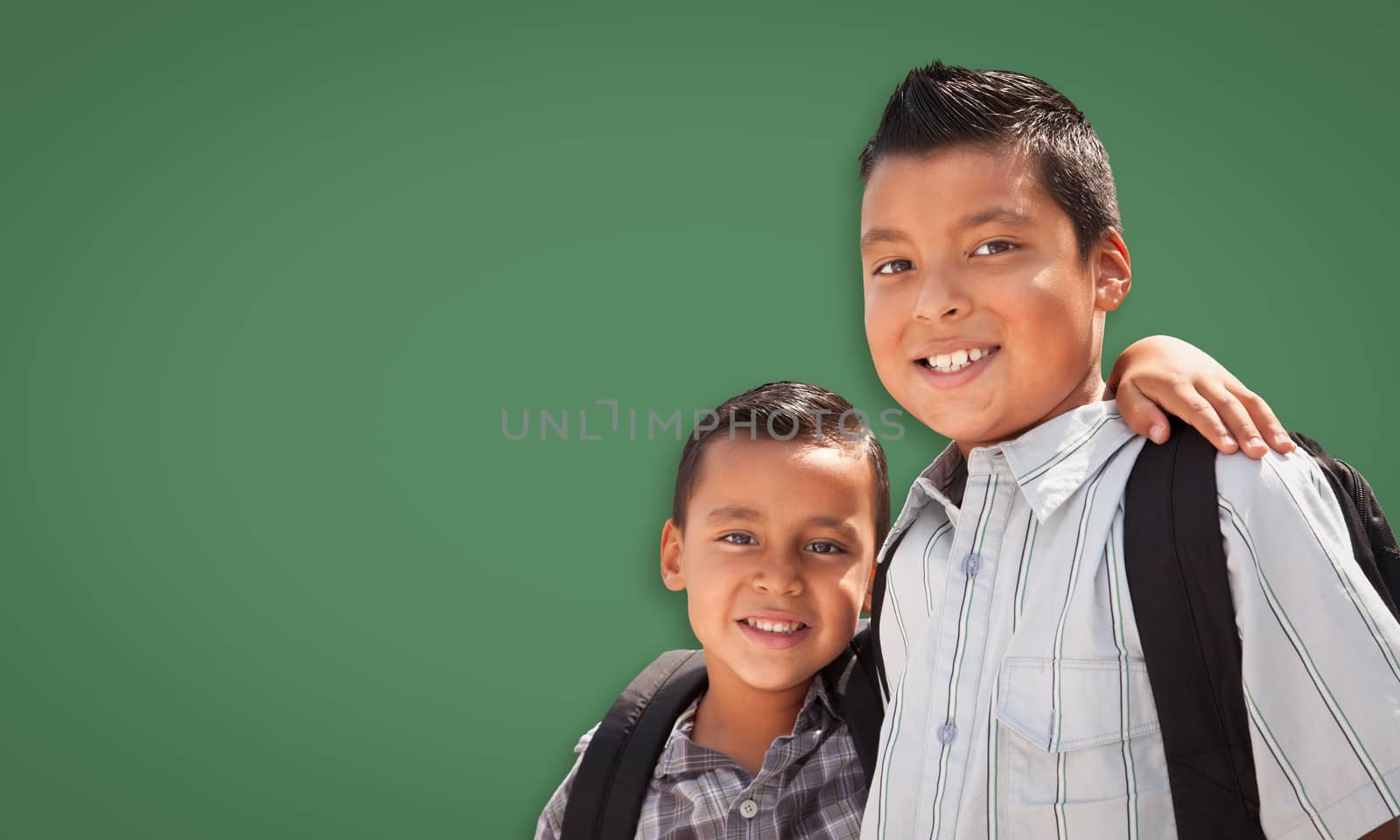 Cute Hispanic Boys Wearing Backpacks In Front of Blank Chalk Board.