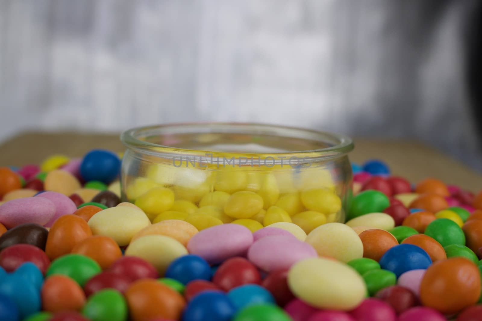 Tasty yellow candies in small jar near colorful sweets around.