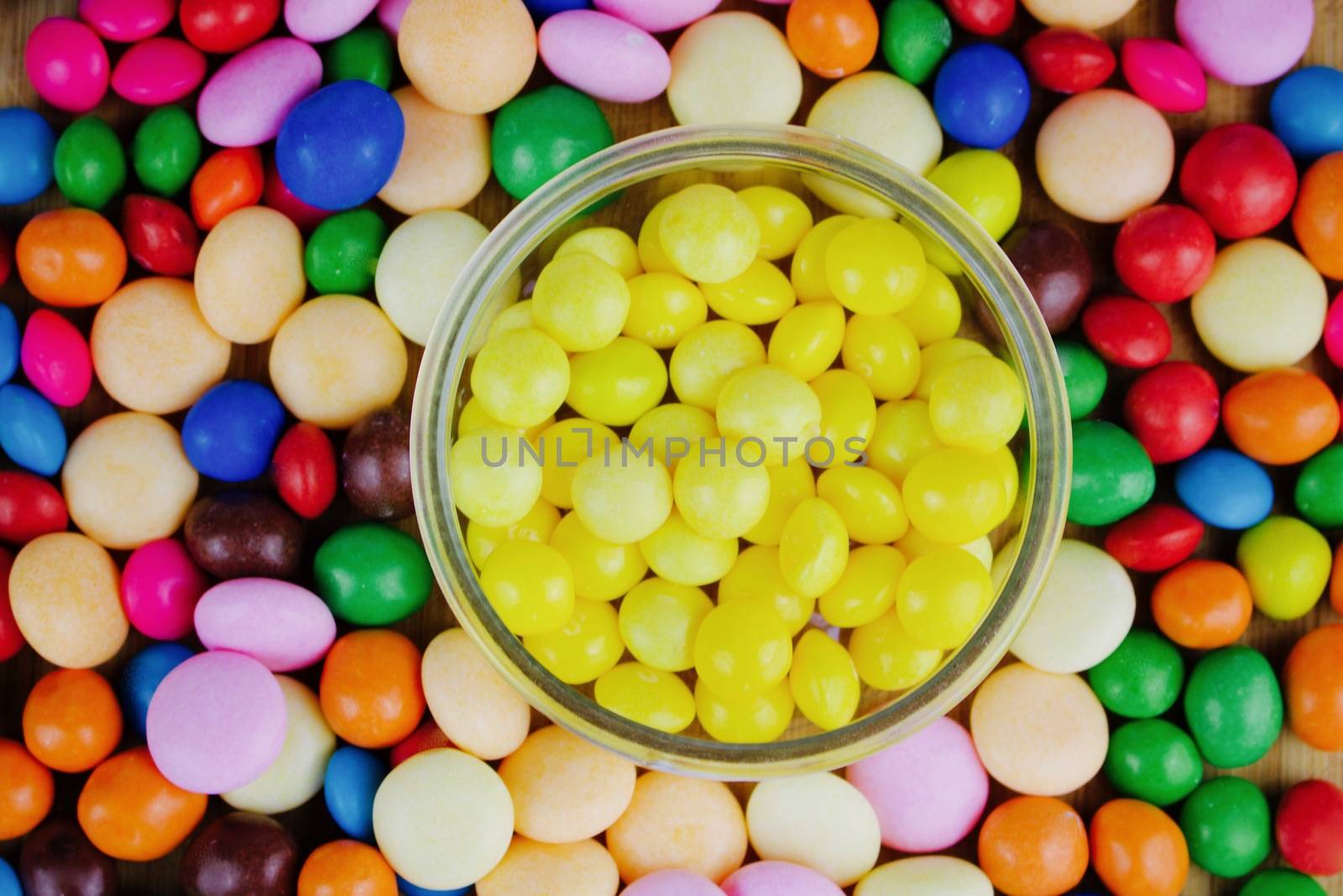 Small yellow sweets in the jar near colored sweets.
