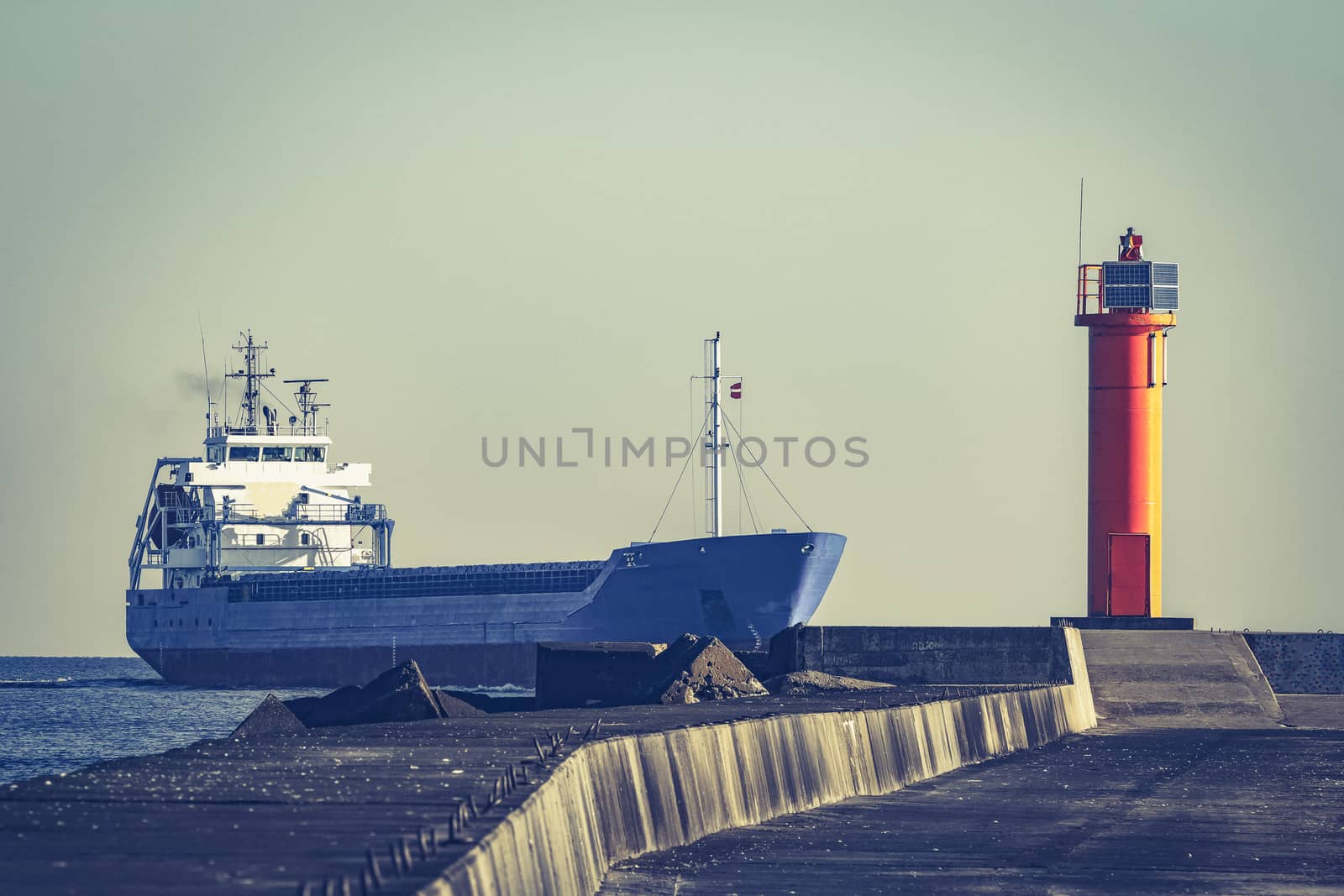 Blue cargo ship sailing against the breakwater dam